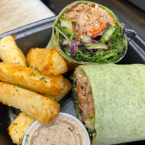 Two halves of a chicken wrap with lettuce, carrots, and cucumber, served with seasoned potato wedges and dipping sauce.