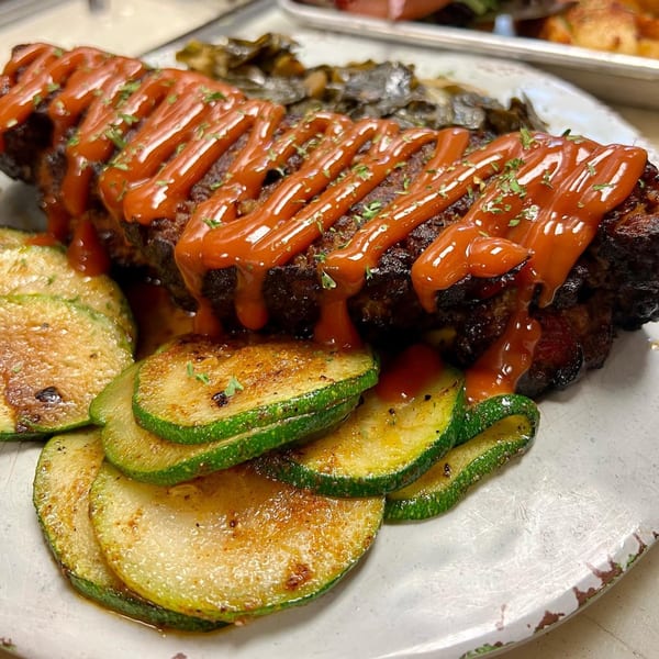 Meatloaf with ketchup drizzle and parsley, served with roasted zucchini slices and collard greens.