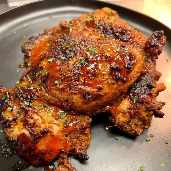 Two pieces of grilled chicken with a shiny orange glaze and green herbs on a dark plate.